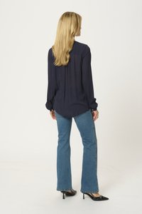 Blouse bleu marine à manches longues avec des poignets boutonnés et une coupe décontractée. Assortie à un jean évasé bleu clair et des talons aiguilles noirs.