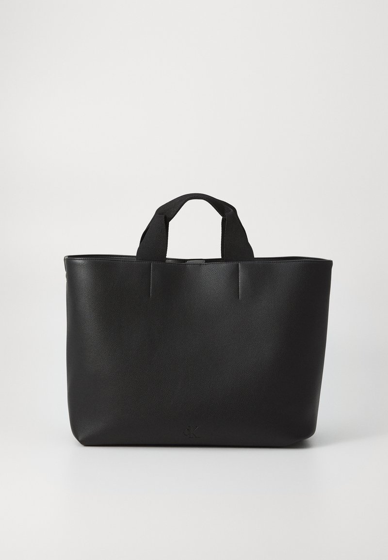 Sac fourre-tout noir avec une finition en cuir lisse, deux poignées en tissu courtes et un design minimaliste. Présente un logo discret sur le bas à l'avant.