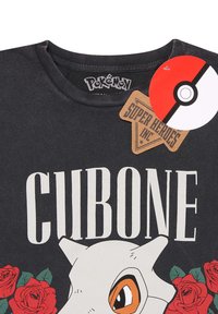 Zwarte katoenen t-shirt met een Cubone-afbeelding, grote witte tekst met de tekst "CUBONE," en rode rozenillustraties. Tags omvatten Pokémon en Super Heroes Inc.