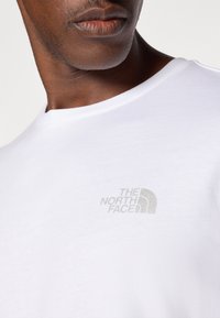 Hvid bomulds t-shirt med rund hals, prydet med et lysegråt broderet logo på venstre bryst. Glat tekstur, kortærmet.