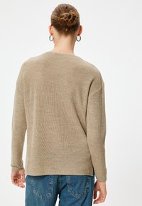 Beige gestrickter Pullover mit langen Ärmeln und lockerer Passform, mit weitem Ausschnitt und geripptem Textur, kombiniert mit blauen Jeans.