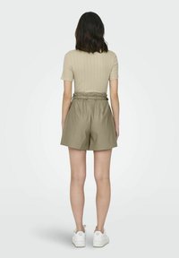 Top corto de manga corta ribeteado color beige combinado con pantalones cortos de talle alto en verde oliva, con un detalle de cinturón y una textura lisa y suave. Zapatillas blancas.
