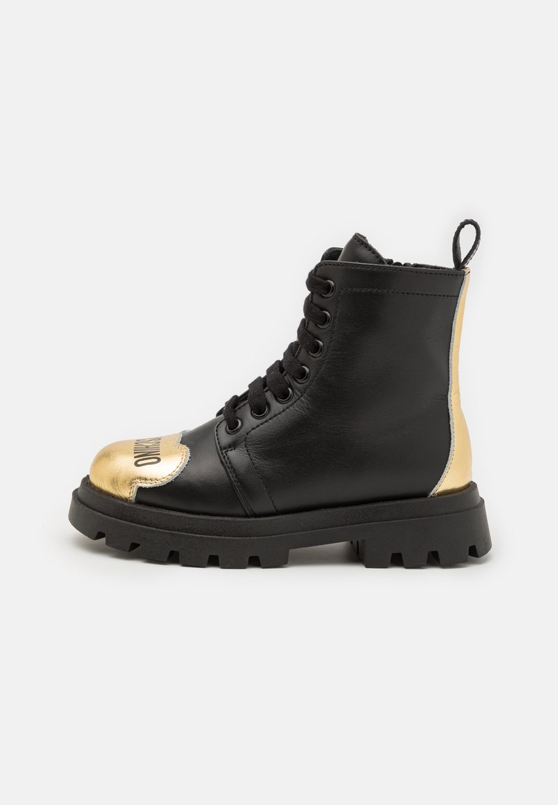 Botín de cuero negro hasta el tobillo con una puntera dorada, cordones negros y una suela texturizada. Presenta un acento dorado en el tacón. Diseño elegante.