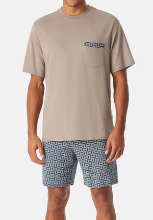 Beige T-Shirt mit kurzen Ärmeln und einer gemusterten marineblauen Tasche, kombiniert mit blauen Shorts, die ein geometrisches Design in Hell- und Dunkelblau aufweisen.