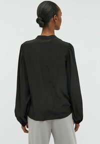 Svart långärmad blus med knäppt krage. Mjukt tyg, samlad detalj vid axlarna och avslappnad passform. Enkel, minimalistisk design.
