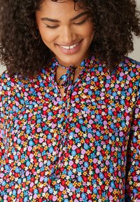 Bloemige blouse met een kleurrijke print op een zwarte achtergrond, met een hoge kraag en strikdetail, korte mouwen en een losse pasvorm.