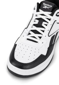 Biele a čierne tenisky Reebok s bielymi šnúrkami a perforáciami v oblasti prstov, na jazyku s viditeľným logom značky.