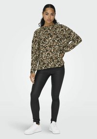 Langærmet blomstrede top med brune, grønne og cremefarvede mønstre; parret med sorte leggings og hvide sneakers. Ensfarvet baggrund.