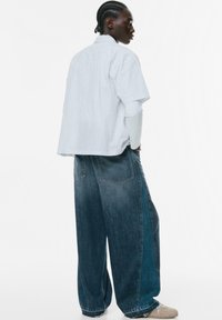 Kratkih rukava bijela majica s tankim plavim prugama, u kombinaciji s velikim tamnim trapericama. Odjeća ima opušteni kroj i minimalistički dizajn.