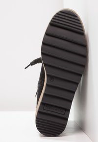 Suela de zapato negra con surcos texturizados, borde de goma clara, estampada con "Tamaris". Talla 37 visible en la parte inferior.