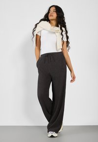 Pantalons larges à côtes gris avec taille élastique à cordon, associés à un t-shirt ajusté blanc et un léger pull drapé sur les épaules.