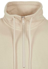 Felpa beige con zip e collo alto, mostrata in primo piano con un focus sui dettagli della zip e del collo.