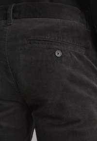 Pantalon en velours côtelé noir avec des côtes verticales, poche avant et un accent en bouton métallique. La texture est douce et durable.