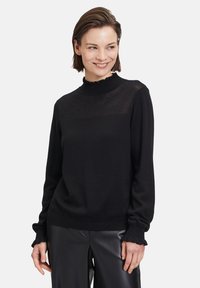 Schwarzer Pullover mit geripptem Kragen, strukturiertem Oberteil und Rüschensäumen. Weicher Stoff mit lockerer Passform und langen Ärmeln.
