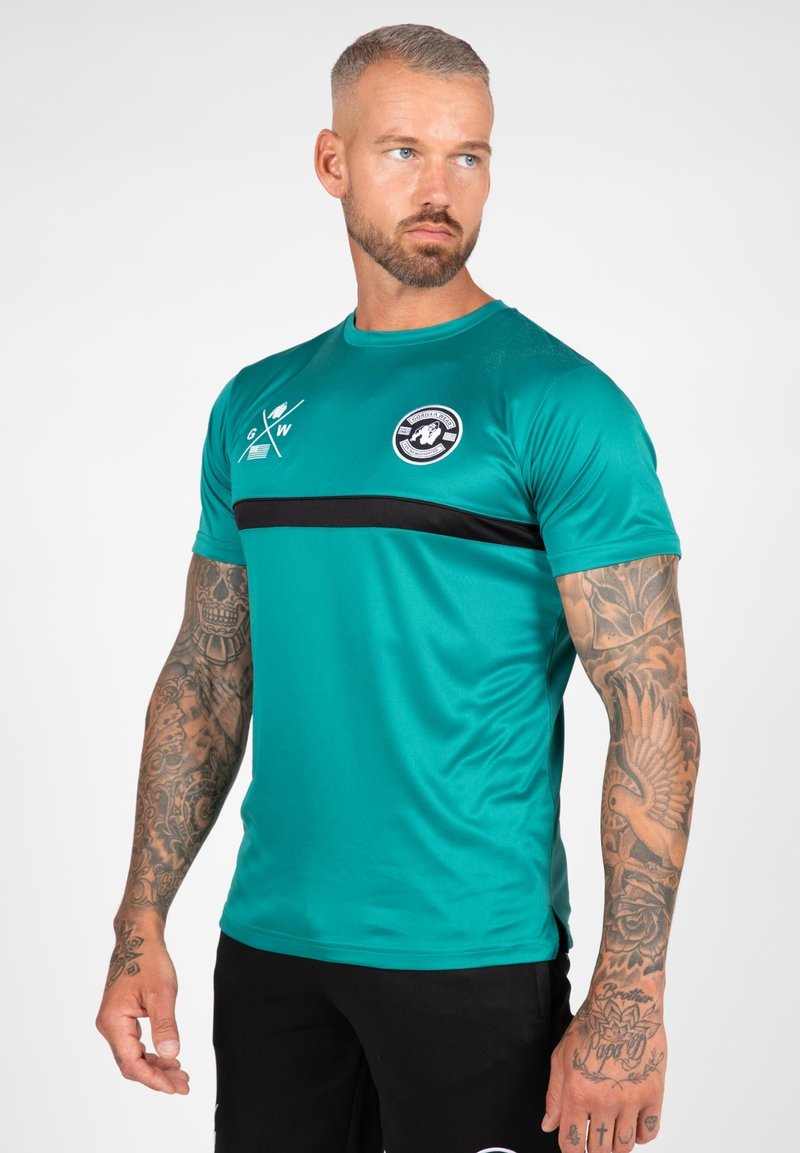 Turkooise sport T-shirt met een zwarte horizontale streep, ronde halslijn en logodetail. Gemaakt van gladde, lichte stof.