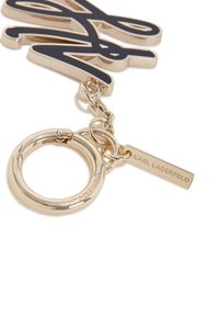 Zlatni privjesak za ključeve s crnim ispisanim logotipom i oznakom na kojoj stoji "KARL LAGERFELD", s glatkom metalnom teksturom i poliranim završetkom.