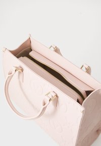 Sac fourre-tout structuré rose en cuir texturé, avec logo embossé, doubles poignées supérieures et intérieur zippé avec des compartiments.