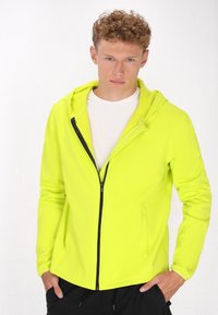 Neon gele zip-up hoodie met een getailleerd ontwerp, capuchon en zijzakken, voorzien van een contrasterende zwarte rits voor extra detail.