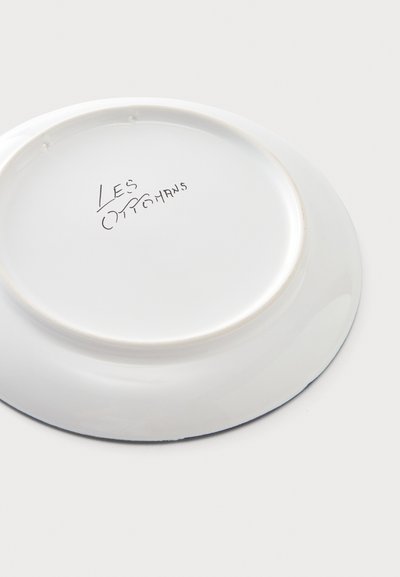 Assiette en céramique blanche présentée à l'envers avec un texte manuscrit "Les Ottomans" au centre en bas.
