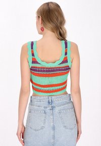 Horgolt cropped top menta zöld, narancs és lila csíkokkal. Kerekített nyakkivágással és nyitott hátrésszel rendelkezik. Magas derekú farmer szoknyával párosítva.