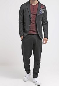 Blazer nero con dettagli in patch, maglietta henley bordeaux, pantaloni neri a sigaretta e sneakers bianche. Design casual e moderno con textures a contrasto.