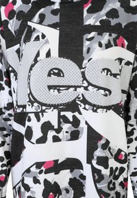 Futuristischer, abstrakter Stoff mit Tierdruck in Schwarz, Weiß, Grau und Pink, der große, silberne Buchstaben mit dem Wort "Ja" in der Mitte zeigt.