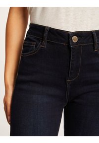 Donkerdenim jeans met een aangesloten silhouet, voorzien van een sluiting met knopen aan de voorkant, riemlussen en contrasterende oranje stiksels langs de naden.