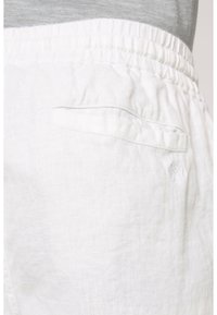 Pantalon en lin blanc avec une ceinture élastique, doté d'une petite poche arrière et d'une texture subtile. Sans ornements ni motifs visibles.