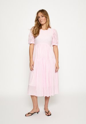 Vestido midi rosa con mangas cortas abullonadas, con un patrón de rejilla texturizado y una falda a capas. Combinado con chanclas negras.