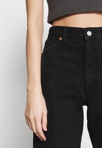Mustat denim-farkut, joissa on korkea vyötärö, napilla kiinnitys, viisi taskua ja hienovaraiset ompeluyksityiskohdat. Tasainen rakenne.