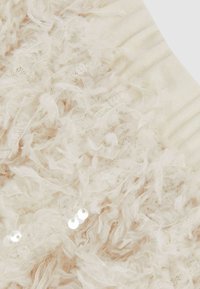 Tissu beige clair texturé avec des fibres douces et effilochées, parsemé de sequins et d'un bandeau élastique côtelé. Apparence douce et superposée.