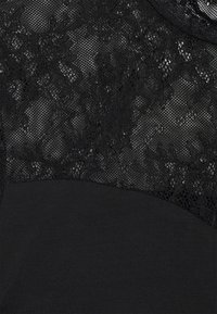 Svart topp med en texturerad spetsöverdela med blommönster som övergår till ett slätt svart nederdel.