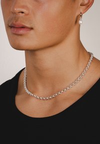 Sølv kædehalskæde med ovale led, parret med en perle-dropørering. Modellen har en sort t-shirt med rund hals på. Glat, poleret finish.
