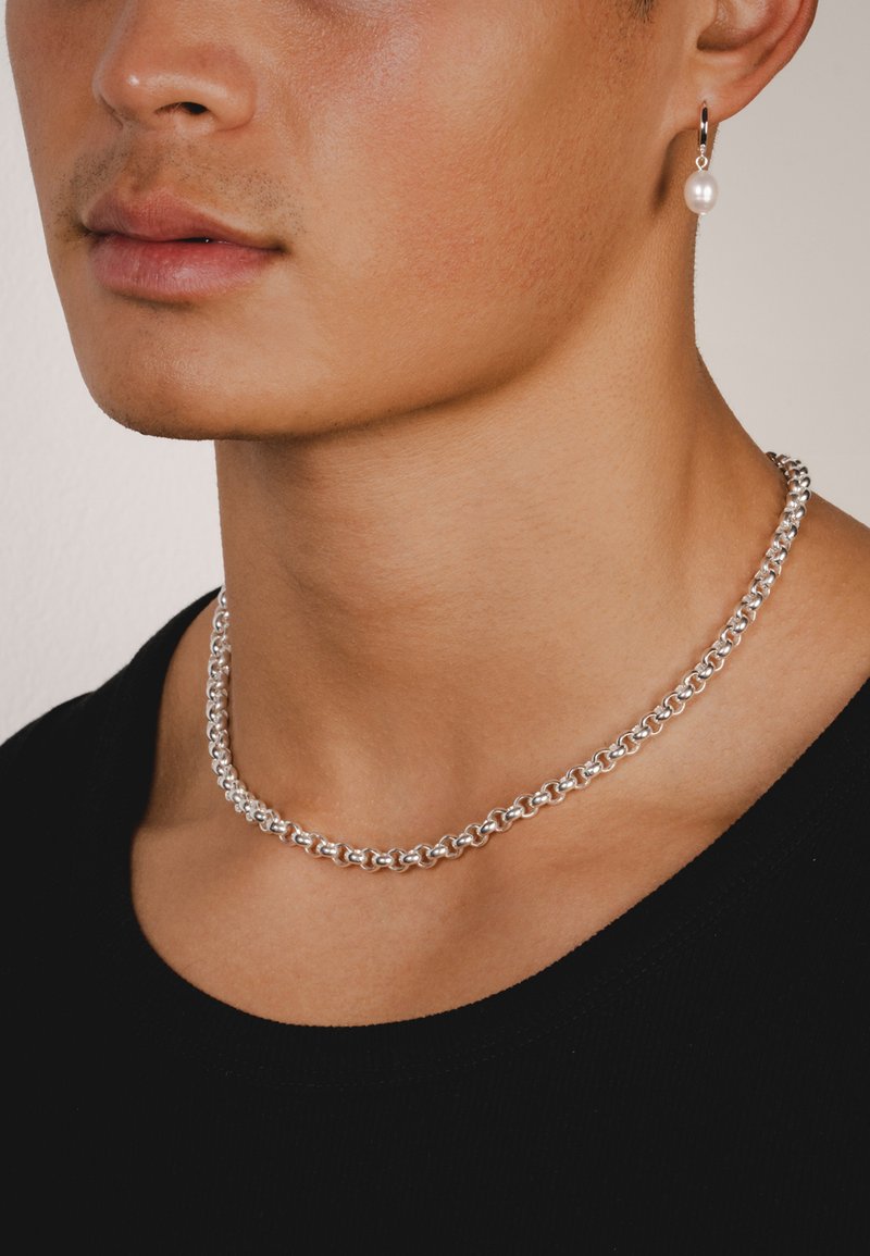 Sølv kædehalskæde med ovale led, parret med en perle-dropørering. Modellen har en sort t-shirt med rund hals på. Glat, poleret finish.