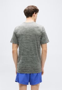 Γκρι αθλ ητική μπλούζα με ελαφρύ μαρμαρυγιακό υφή, στρογγυλή λαιμόκοψη και κοντά μανίκια, εμφανίζεται δίπλα σε μπλε σορτς.