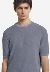 Kortärmad, ljusblå stickad tröja med en texturerad, ribbad mönstring och en rund halsringning med en kontrasterande kant.