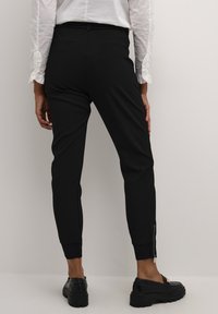 Pantaloni neri su misura con una forma aderente, tasche laterali e dettagli con zip alle caviglie, realizzati in un tessuto liscio e elasticizzato.
