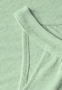 Světlé zelené texturované látky s kulatým výstřihem a viditelným švem, složené pro jasný pohled na límec a materiál.