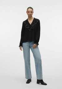 Sort langærmet bluse med flæsekrave og hvid kant, parret med lyseblå vide jeans og sorte hælede ankelstøvler.
