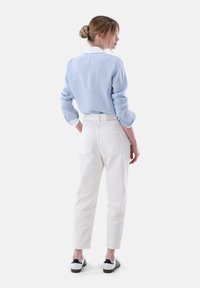 Blue striped shirt with white collar, paired with white high-waisted pants and black and white sneakers. Model shown from the back.