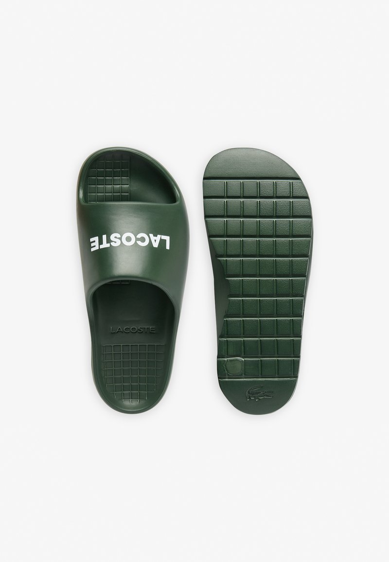 Grüne Gummischlittschuhsandale mit einem breiten Riemen, der das "LACOSTE"-Logo trägt, strukturiertem Fußbett und gemusterter Sohle für besseren Halt.