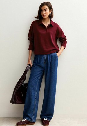 Bordeaux lange mouw polo met een kraag, gecombineerd met hoge taille, wijde blauwe denim jeans. Bruine sneakers en een donkere tas maken de look compleet.