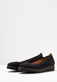 Bailarinas de ante negro con una textura suave, puntera redondeada y ligera elevación. El forro interior es marrón, con un diseño minimalista y sin herrajes visibles.