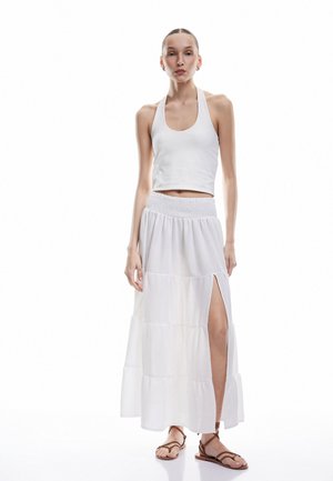 Top corto blanco sin mangas con un cuello alto, combinado con una falda larga blanca de volantes que presenta una abertura lateral, tela texturizada y cintura elástica.