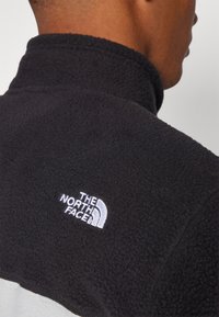 Fleece sweatshirt in zwart met een hoge kraag. Kenmerkt zich door het witte geborduurde logo "THE NORTH FACE" op de schouder. Gelaagde stofoppervlak.