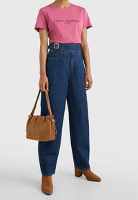 Rosa bomull t-shirt med en svart logotyp, högmidjade blå jeansbyxor, brun läderhandväska och beige klackstövlar.