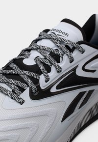 Κοντινό πλάνο λευκού και μαύρου παπουτσιού Reebok με λευκούς και μαύρους κορδόνια με σχέδιο και ορατό λογότυπο Reebok στη γλώσσα και την πλευρά.