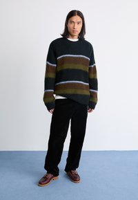 Chunky strikket sweater i mørkegrøn, brun og lyseblå striber; parret med sorte fløjl bukser og bordeaux snørebåndssko med struktureret sål.