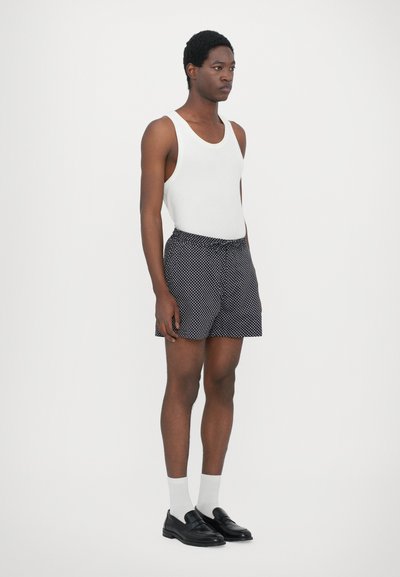 Débardeur blanc, shorts navy avec des pois blancs, chaussures noires et chaussettes blanches. Design simple, coupe décontractée et taille élastique.