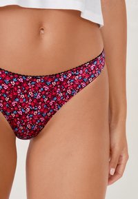 Perizoma con motivi floreali in tonalità di rosso, rosa e blu, con un bordo in pizzo nero. Tessuto morbido per una superficie liscia.